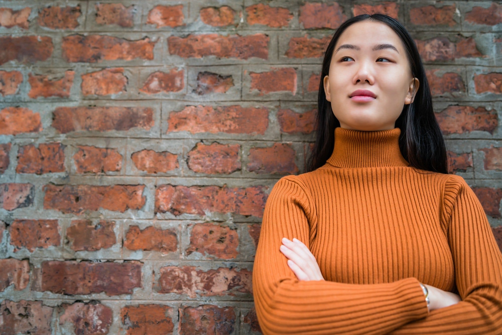 Asian woman against brick wall.