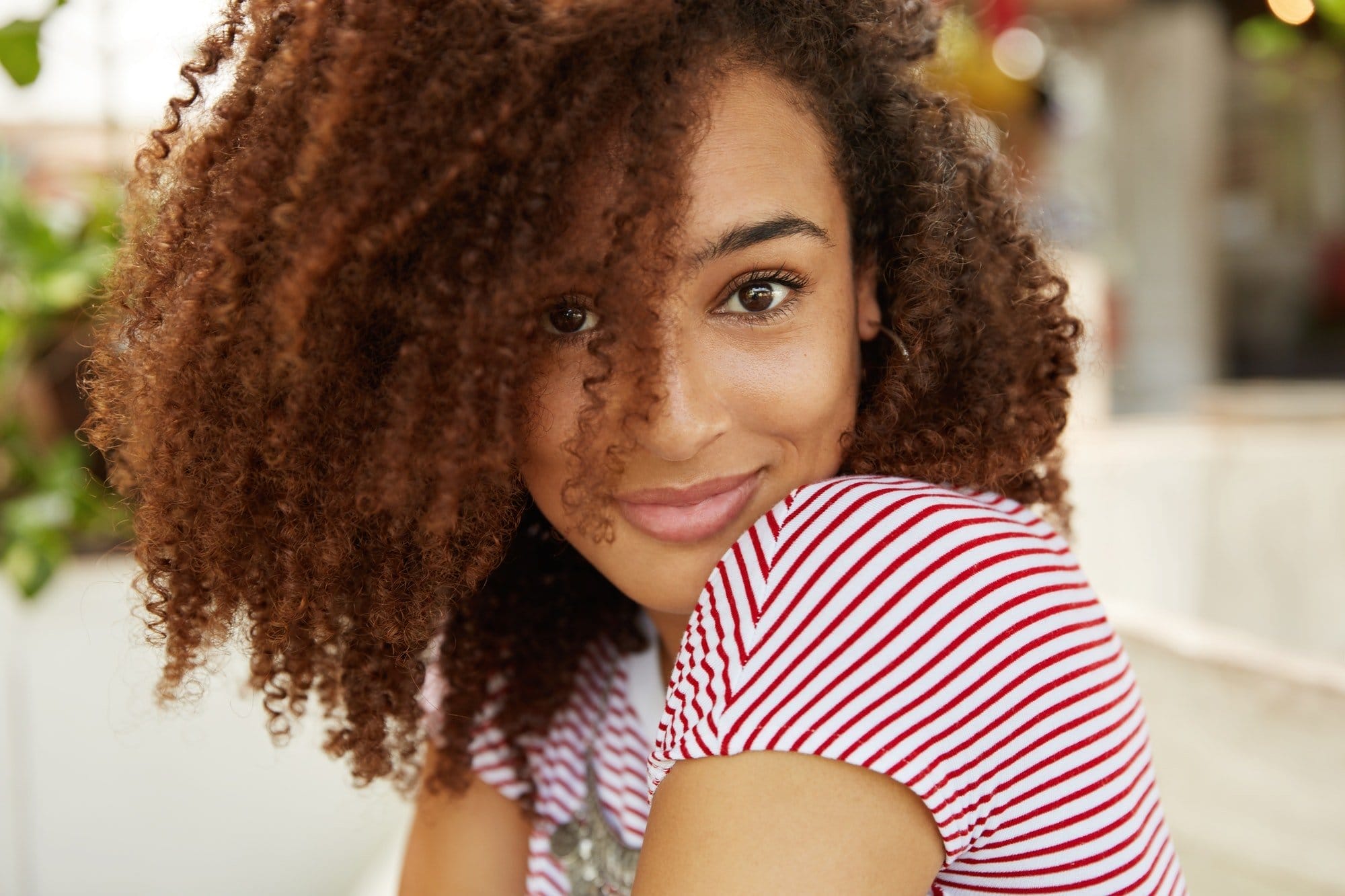 Sideways portrait of stylish female with curly Afro hairstyle and dark skin, being satisfied to achi